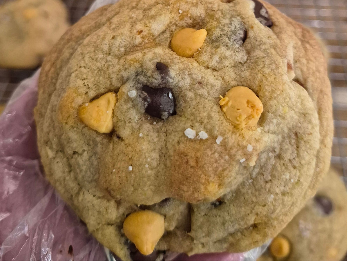 A close-up of a large chocolate chip cookie butterscotch morsels,chocolate chips, and pretzels with coarse sea salt sprinkled on top.